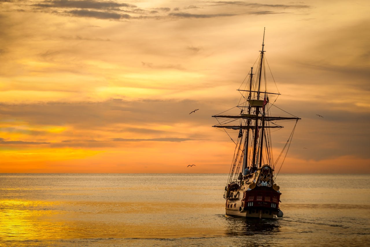 about-img A majestic pirate ship sails into the serene waters at sunset, casting a dramatic silhouette.